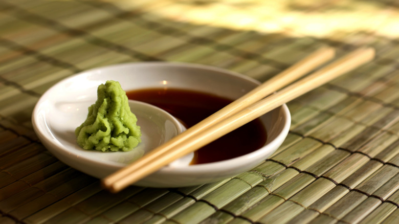 Dish of soy sauce and wasabi with chopsticks on bamboo placemat