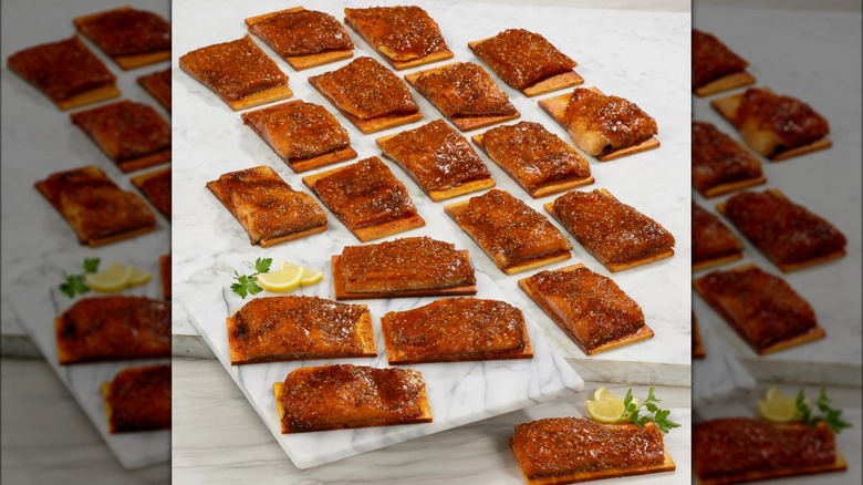 Many portions of salmon fillets on top of cedar planks for cooking.
