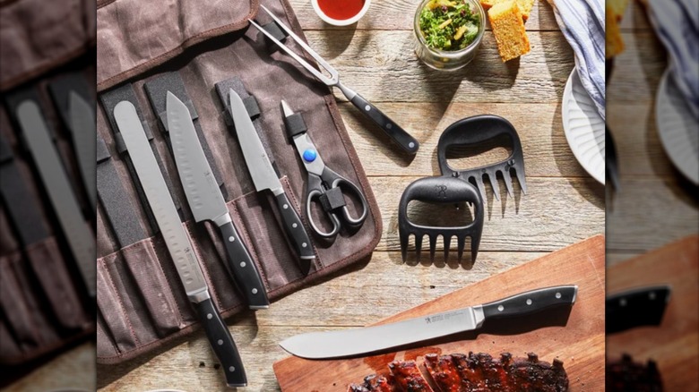 Barbecue utensil set on table with cooked ribs and other foods.