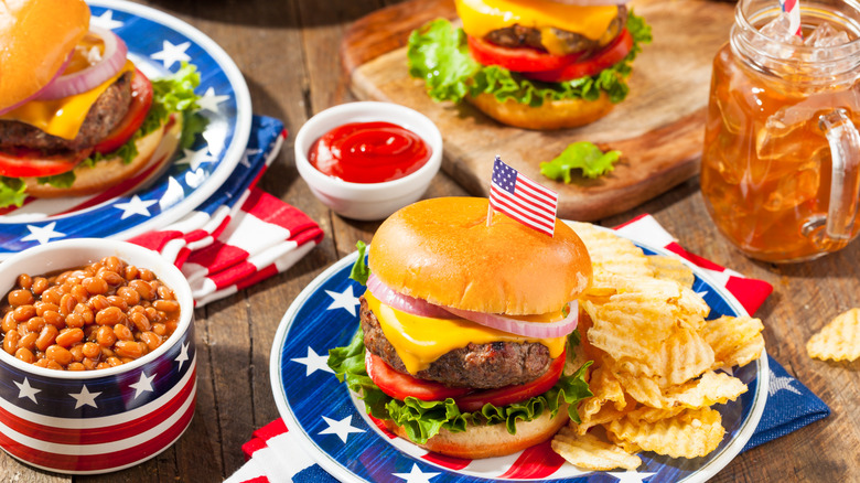 Burgers, beverages, and baked beans on patriotic plates in honor of 4th of July.
