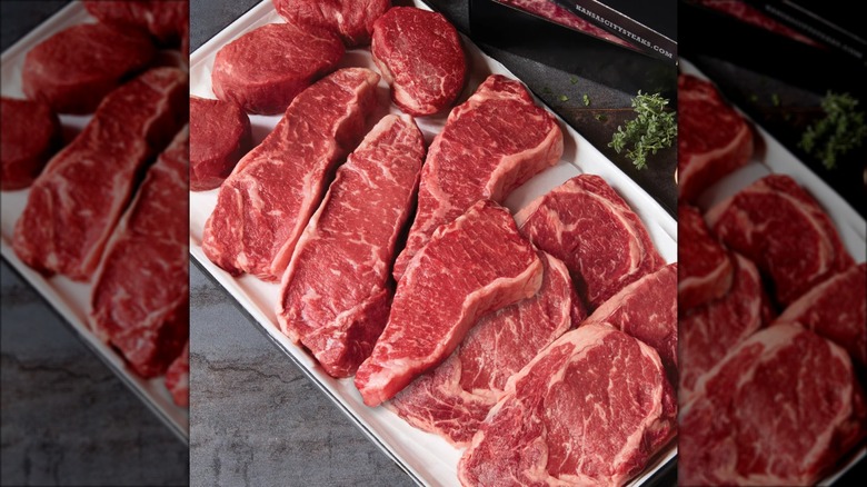 Multiple raw steaks on plastic tray.