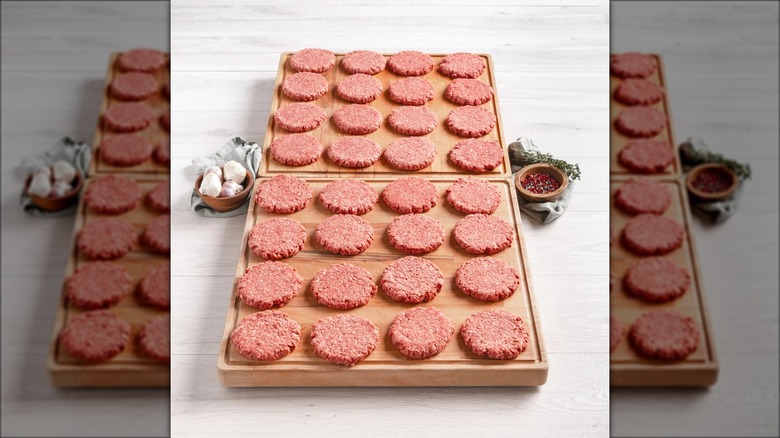 Rows of raw beef patties spread out over two wood cutting boards.