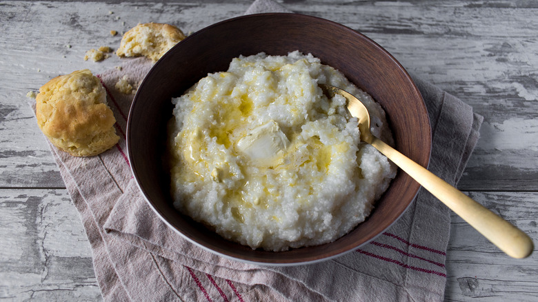 grits with butter in a bowl next to biscuit on rustic table