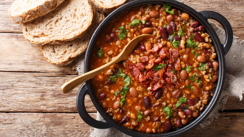 Cast iron pot with soup beans with ham and greens next to slices of bread on rustic table