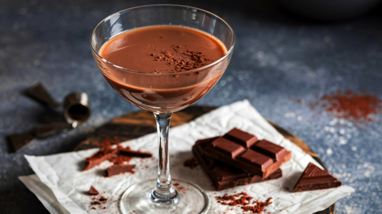A chocolate martini next to some chocolate and cocoa powder