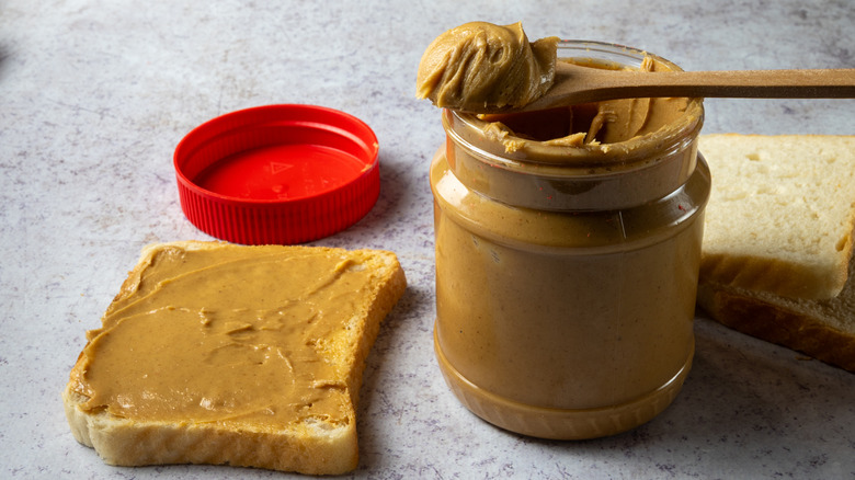 A jar of peanut butter and a slice of bread smeared with peanut butter