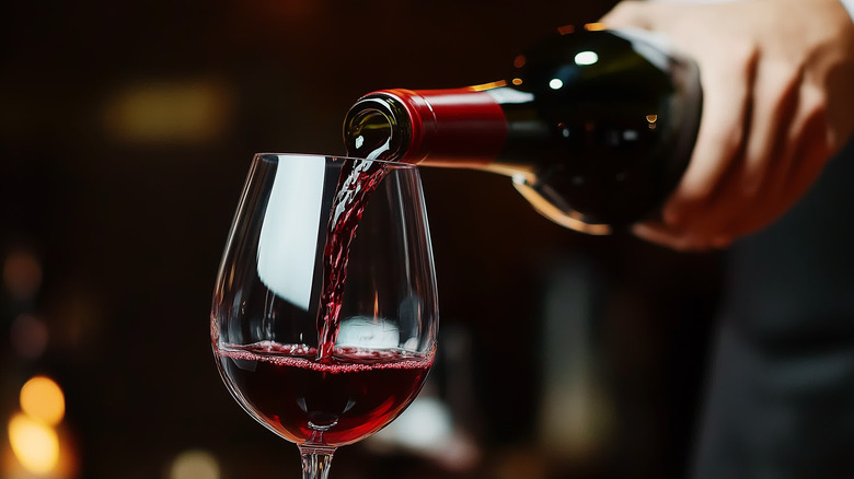 Someone pouring a bottle of red wine into a glass