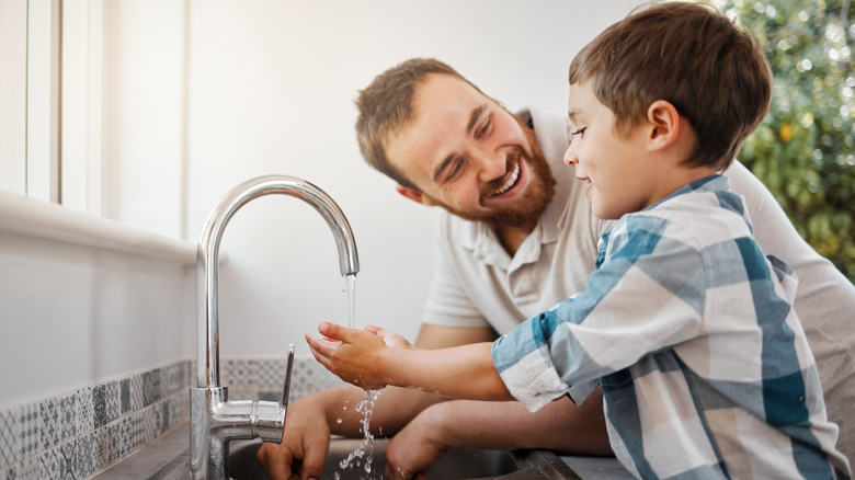 A father smiling while his son washes his hands