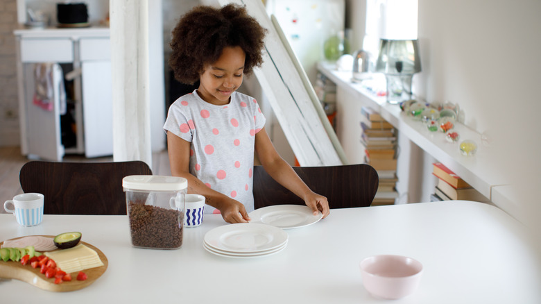 A little girl helping with plates at the dining table