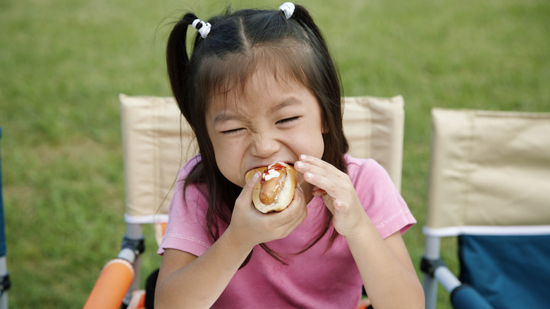 A little girl eating a hot dog outside