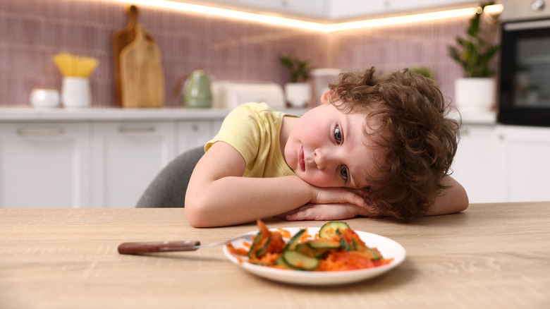Unhappy boy not wanting to eat a plate of vegetables