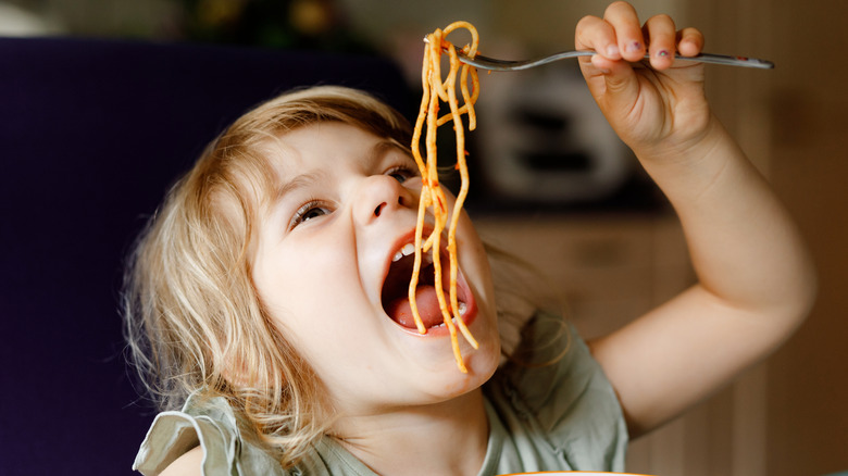 A child dangling spaghetti over her open mouth