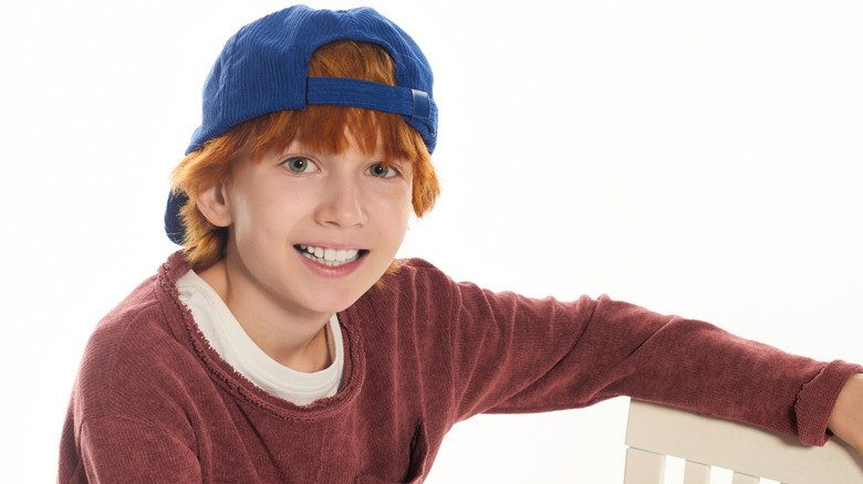 A smiling boy in a baseball cap posing with a chair