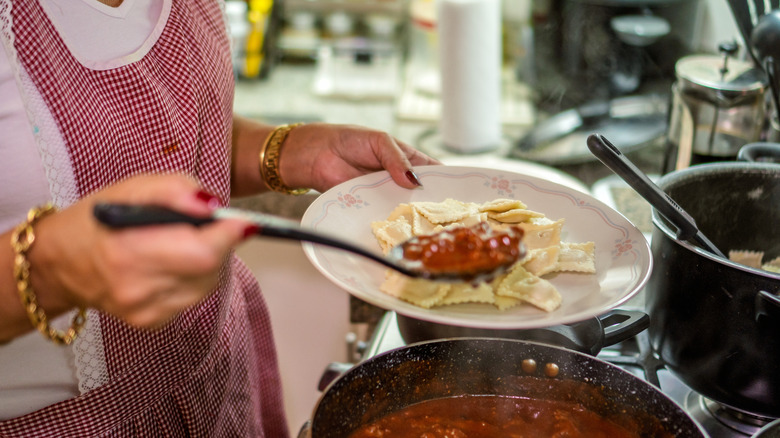 A woman serving a plate of ravioli with meat sauce