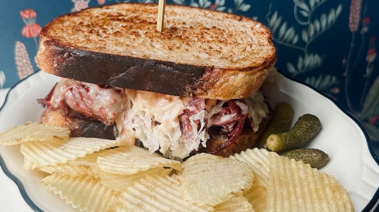 House reuben sandwich, chips, and cornichons on a white plate at Bernie's