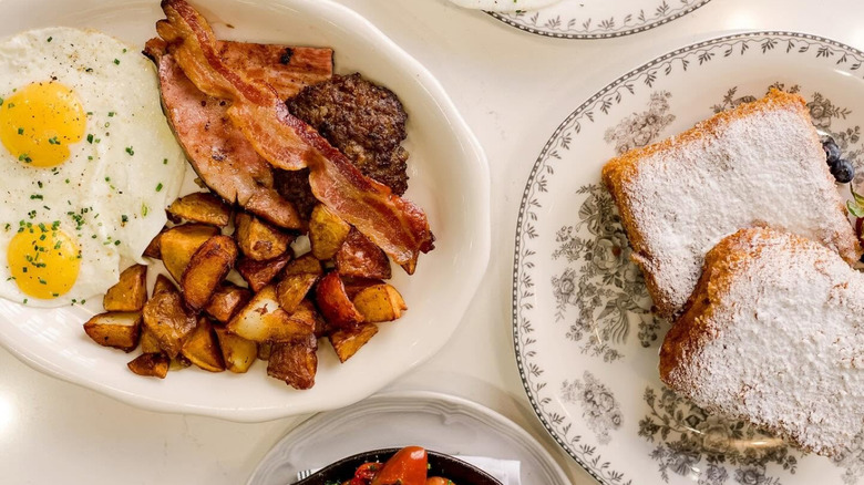 White platter of over eady eggs with bacon and country potatoes and a plate of toast covered in powdered sugar