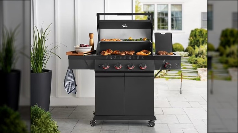 Backyard gas grill on patio with meats and accessories.