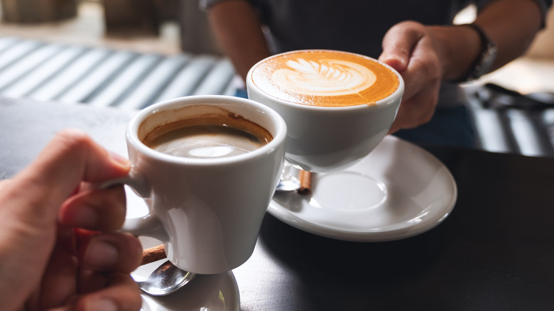 two people clinking cups in a coffee shop