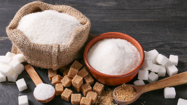 White sugar and brown sugar in bowls, bags and spoons with sugar cubes