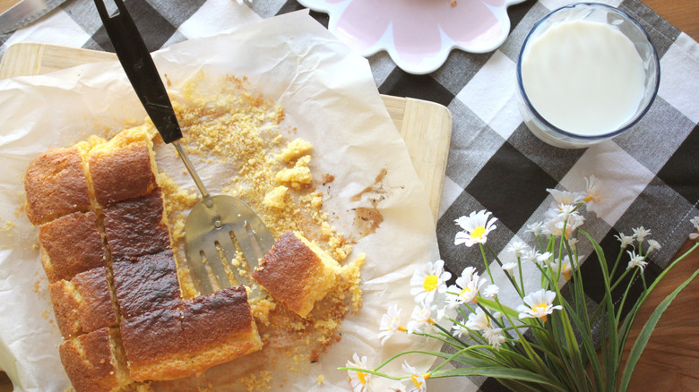 Slices of cornbread on parchment paper next to a glass of milk and daisies