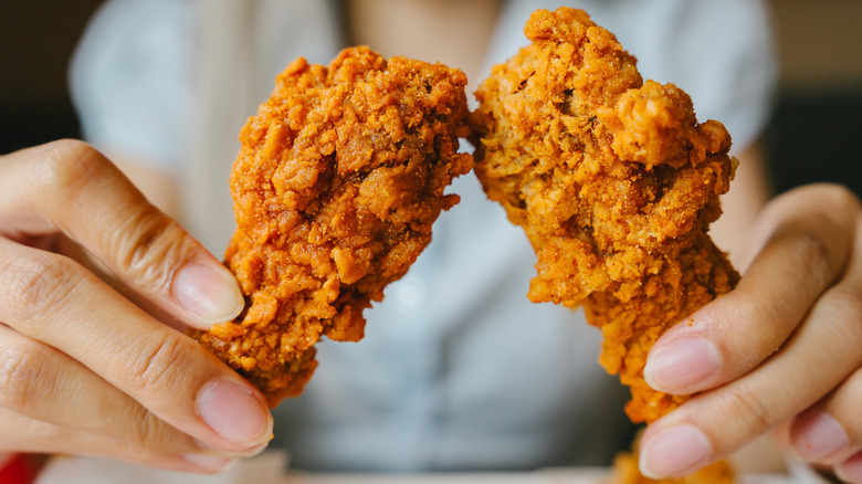 A person holding two fried chicken drumsticks