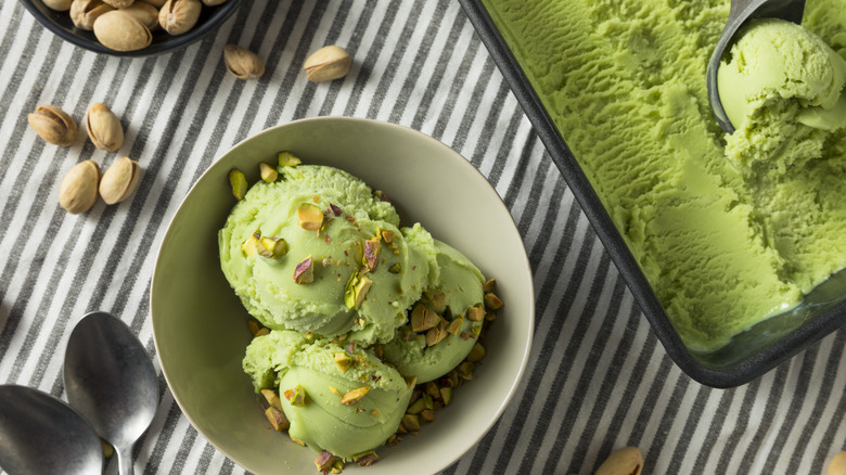 Pistachio ice cream in a white bowl with a tub of ice cream and pistachios