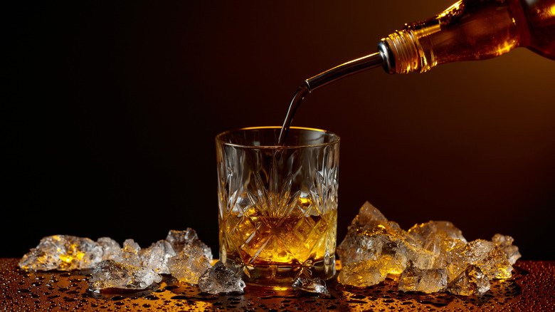 Whiskey being poured from a bottle into a crystal rocks glass, surrounded by melting ice