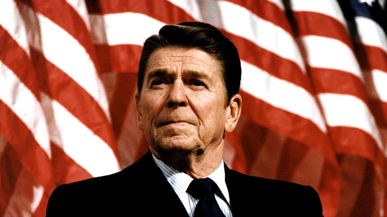 Color portrait of Ronald Reagan in a dark suit, standing in front of an American flag