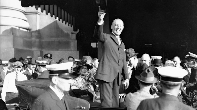 Black-and-white photo of Woodrow Wilson waving to a crowd while surrounded by people