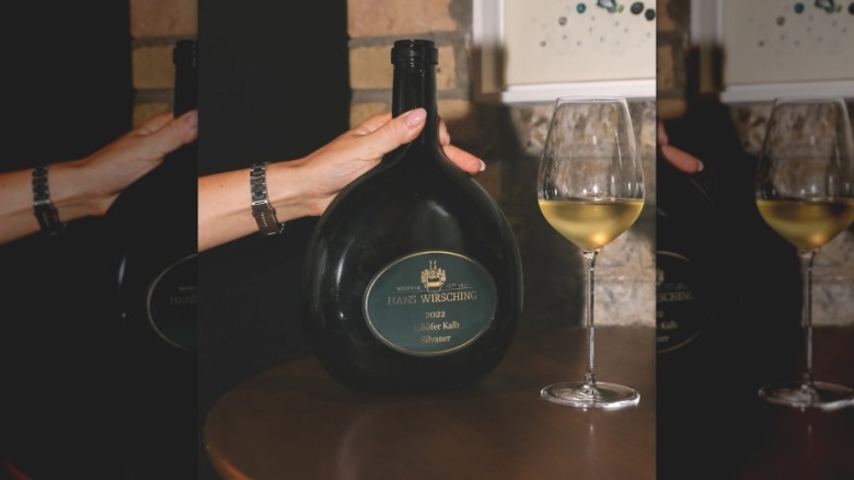 woman's hand holding a bottle of Hans Wirsching Silvaner with glass of white wine next to it