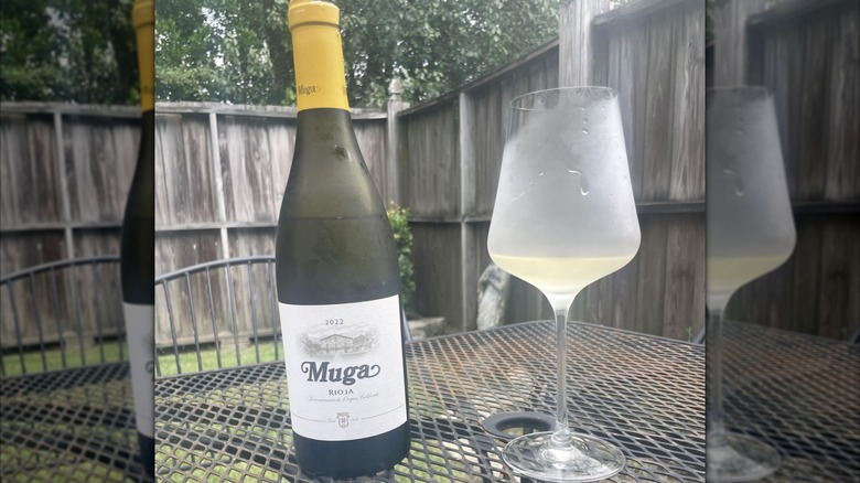 bottle of Bodegas Muga blanco on backyard wire table with frosted glass of white wine
