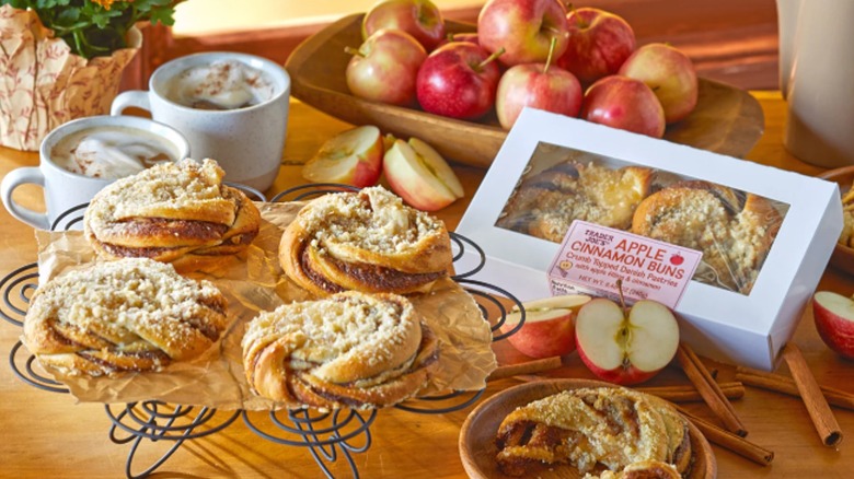 Tray and box of Trader Joe's Apple Cinnamon Buns with apples and drinks on table.