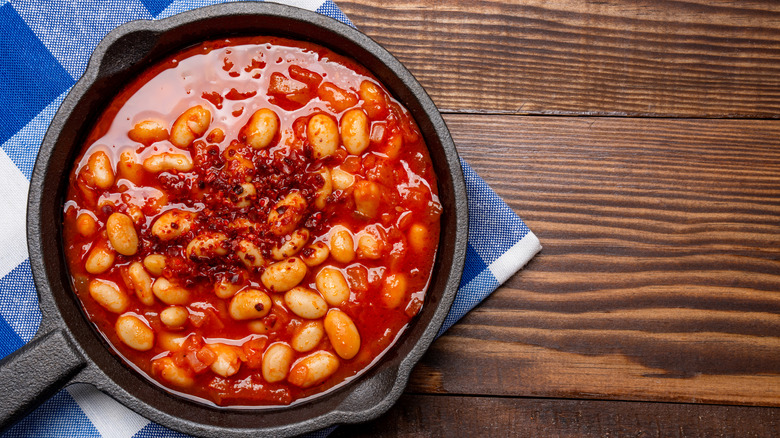 Baked beans in a cast-iron pan on a blue and white tea towel on a wooden surface