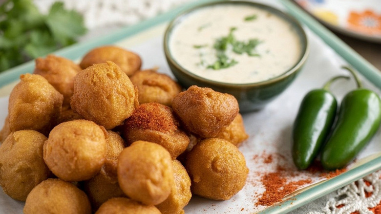 Hush puppies on a white and teal dish with peppers and dip on the side