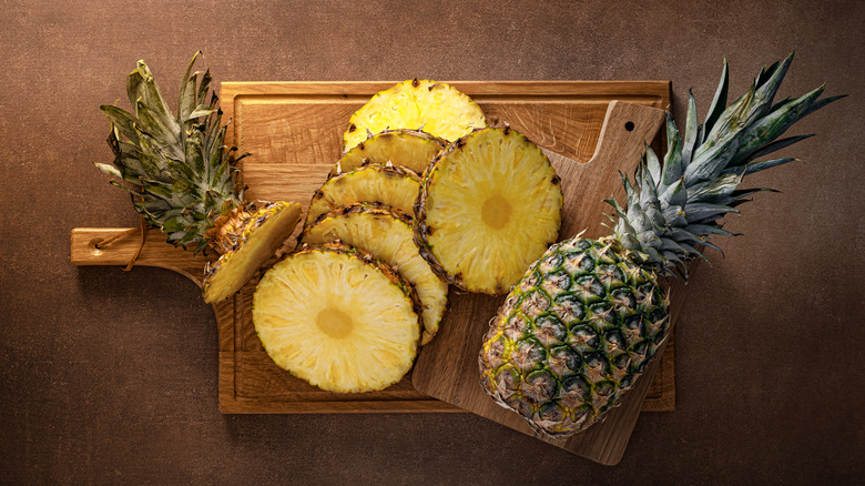 Sliced pineapple on a wooden board with a whole pineapple on the side