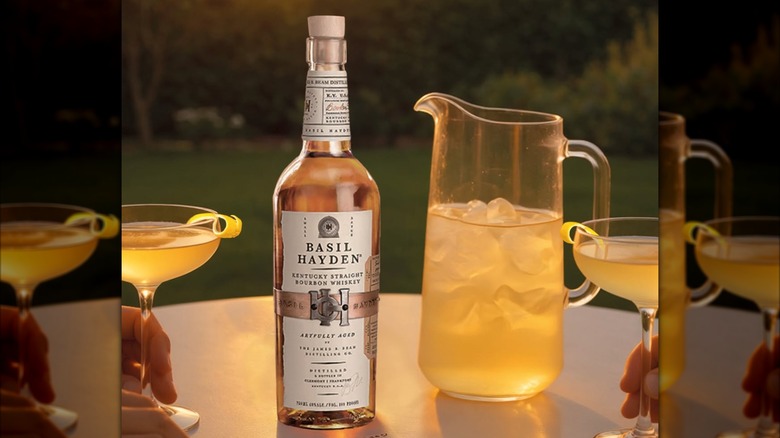 Bottle of Basil Hayden with cocktails and pitcher on table outside at sunset