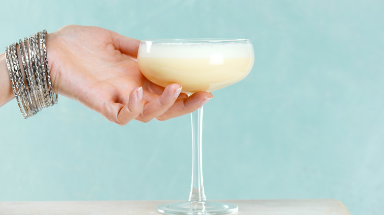 Hand holding frothy cocktail in coupe glass