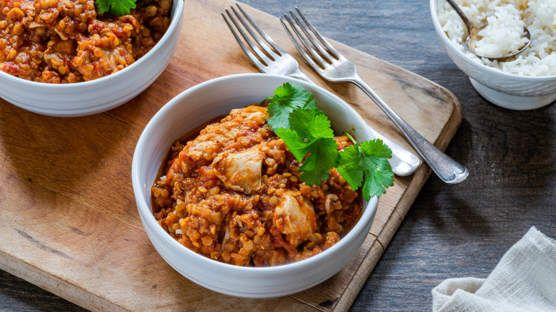 Chicken dhansak in a white bowl on a wooden board with a side of rice