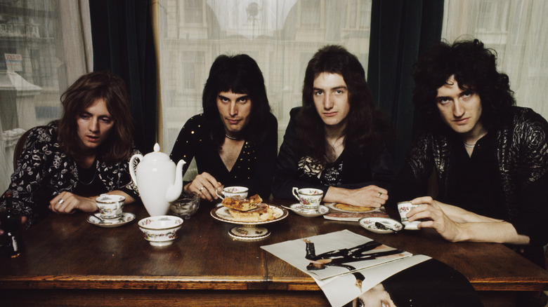 Freddie Mercury with Queen bandmates with tea cups and a teapot at a table
