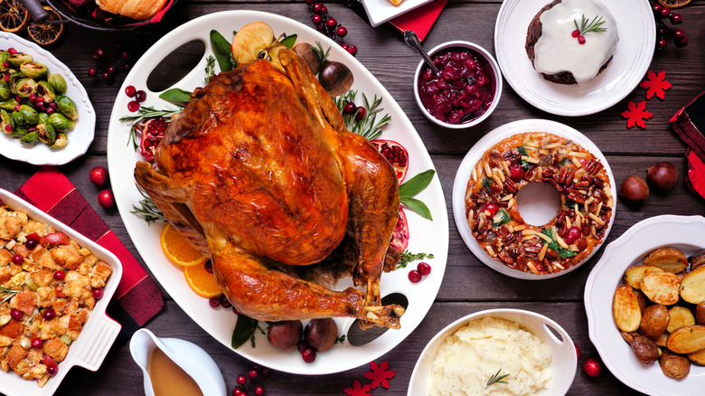 Top view of a Christmas spread including a roast turkey, pudding, mashed potatoes, roasted potatoes, fruitcake, jam, and Brussels sprouts