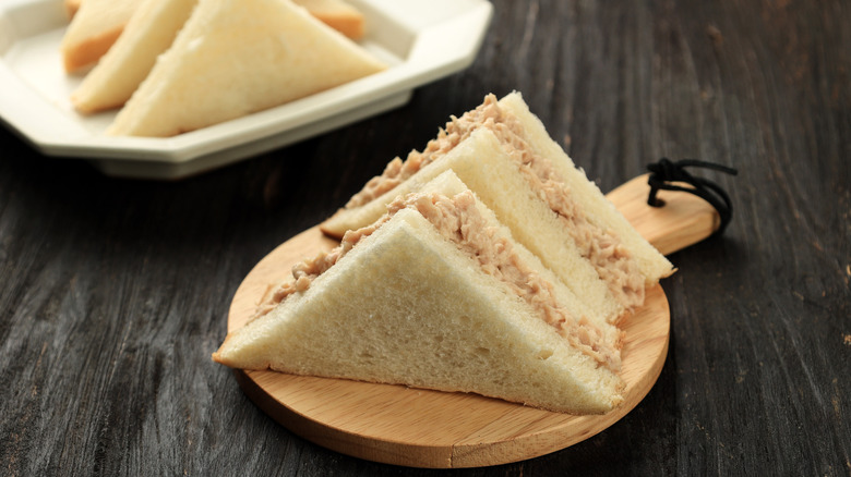 Tuna sandwiches on a wooden serving plate and a white plate