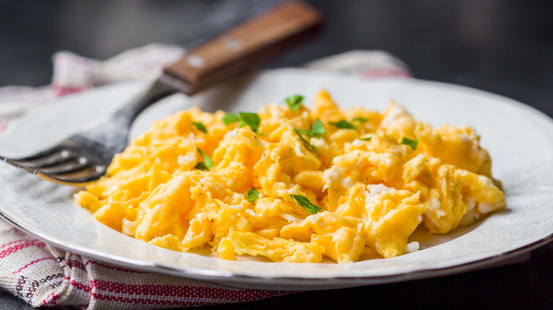 Scrambled eggs with herbs on a white plate with a fork