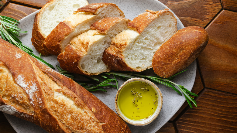 A baguette sliced up with some olive oil dip and fresh herbs