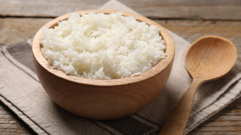 White rice in a wooden bowl next to a wooden spoon