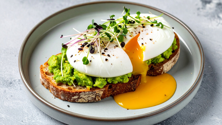 A poached egg broken on top of avocado toast