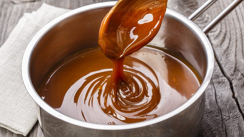 A wooden spoon dipping into a pot of caramel sauce