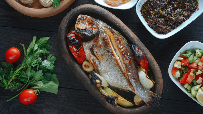 cooked whole fish in a tray surrounded by sides