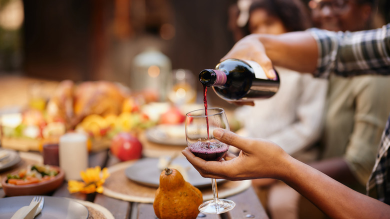 Woman pouring a bottle of red wine into a wine glass with food in background