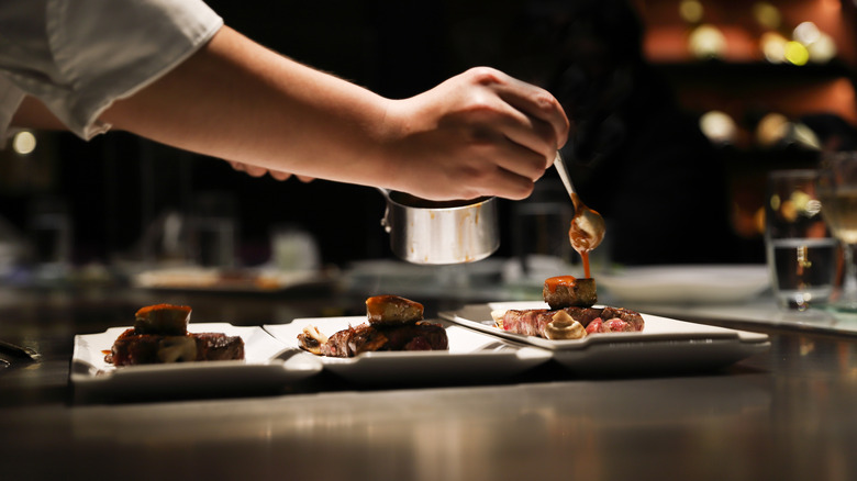 Chef spooning sauce over steak dinner