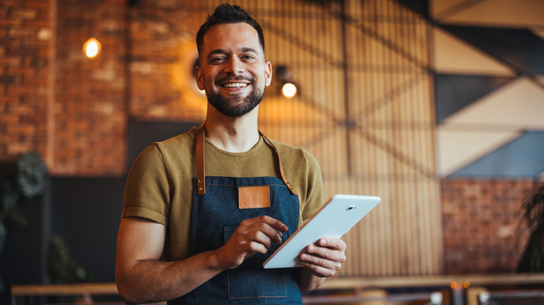 Male waiter wearing an apron and holding a tablet